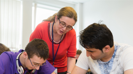 Lecturer supporting two students who are working in a classroom.