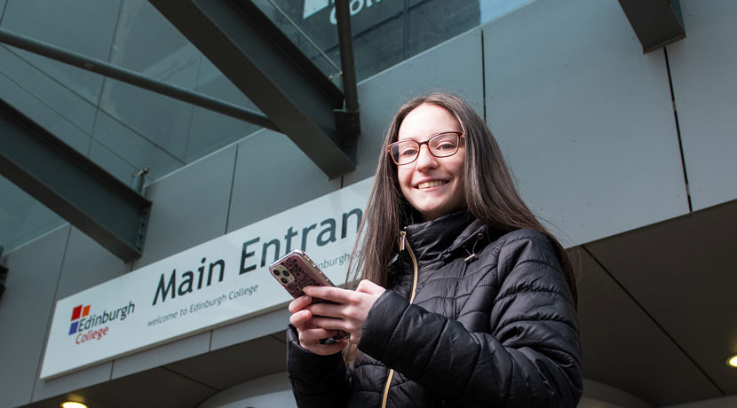 Young student looking at their phone outside a college campus building.