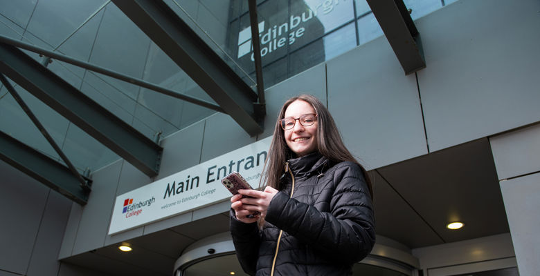 Young student looking at their phone outside a college campus building.