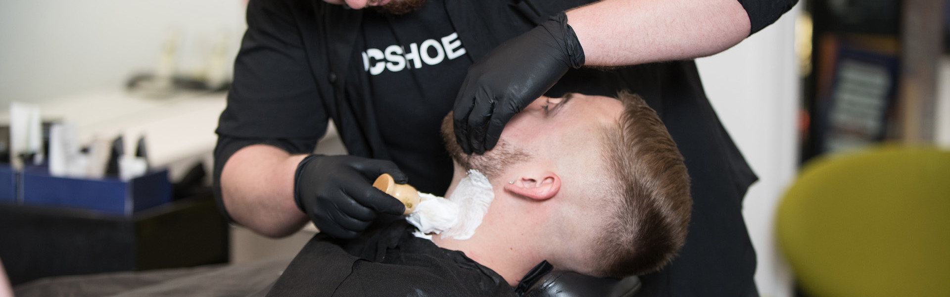 Barbering student applying shaving foam to a client's beard in the salon.