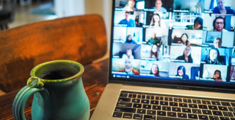 Multiple faces on a screen during a conference call, with a cup of coffee to the side of the laptop.