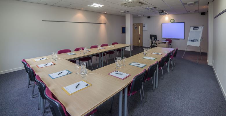 Conference room set up at Edinburgh College, with tables set up in a U shape with notebooks and water on the tables.