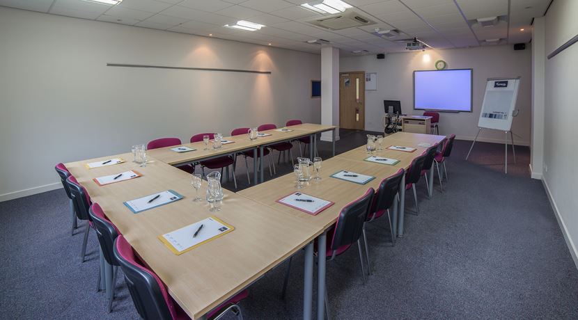 Conference room set up at Edinburgh College, with tables set up in a U shape with notebooks and water on the tables.