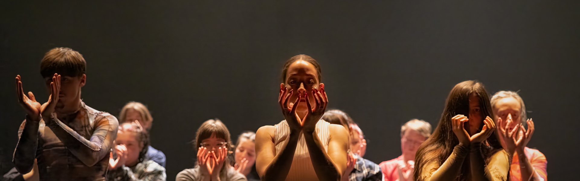 A group of dancers in colorful outfits perform on stage, creating a visually striking scene with dramatic lighting.