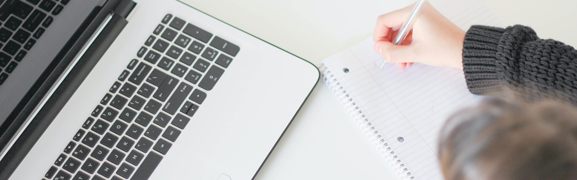 Student writing notes while looking at their laptop.