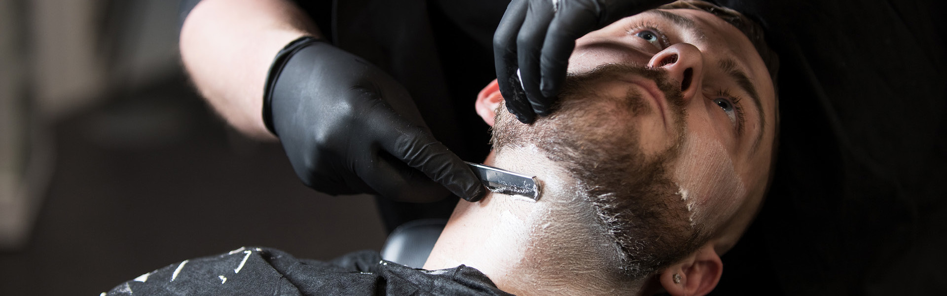 Barbering student shaving a client's beard in the salon.