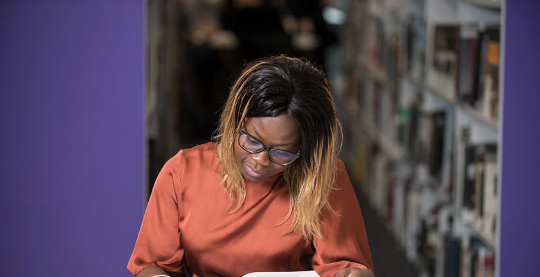 Student in the library reading a book at a desk.