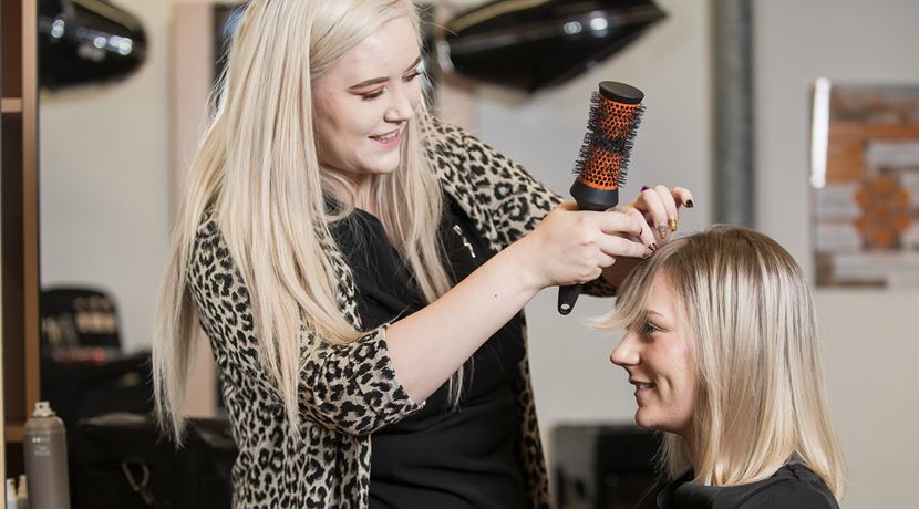 Hairdressing student brushing a client's hair in the salon.