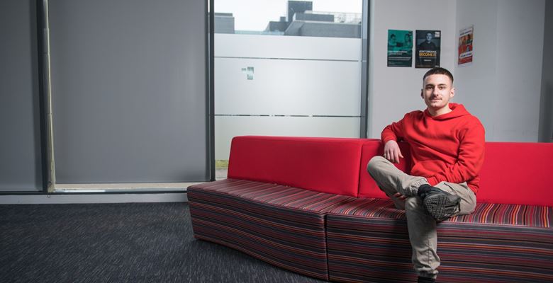 Fabio Scalici sitting on a red sofa at college.
