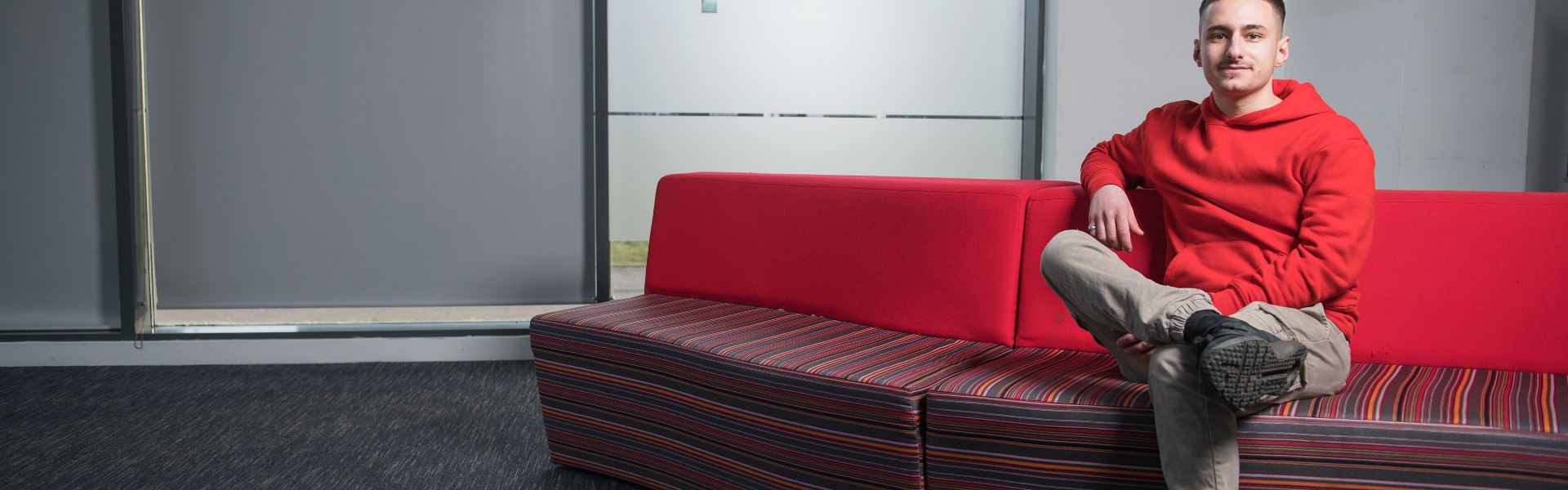 Fabio Scalici sitting on a red sofa at college.