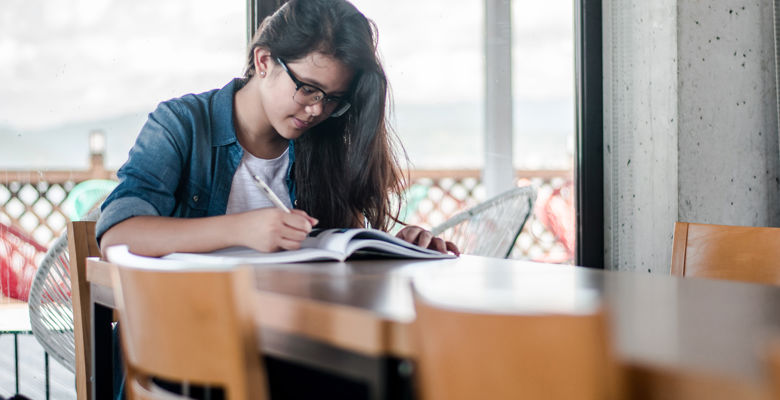 Young student looking through a textbook at a table. 