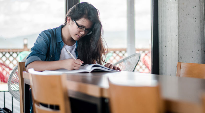 Young student looking through a textbook at a table.