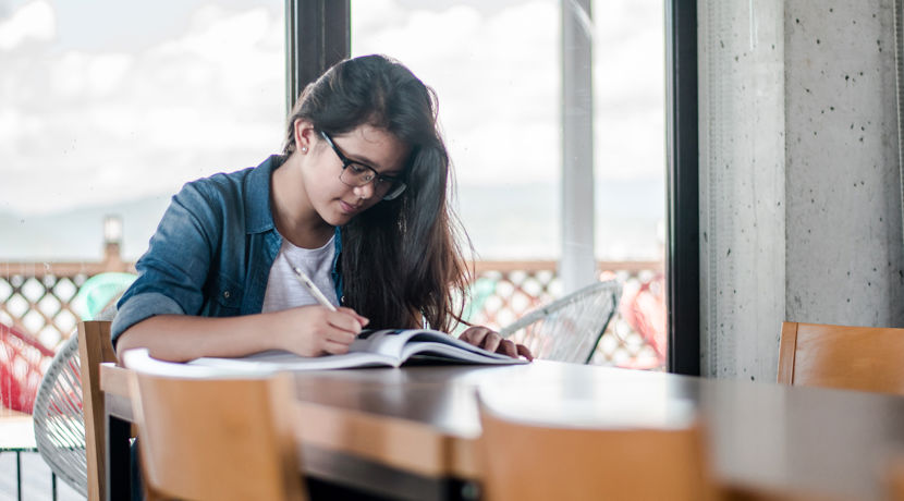 Young student looking through a textbook at a table.