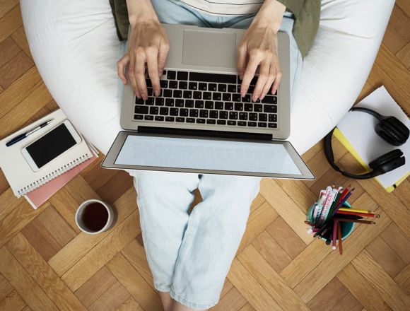Person working on a laptop with notebooks, pens and a cup of coffee surrounding them.